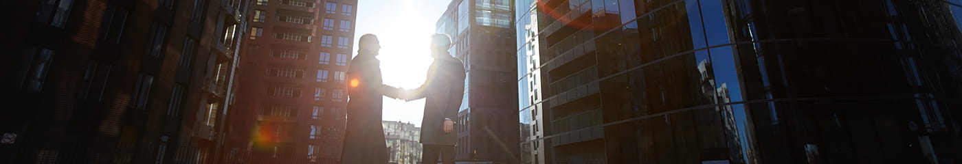 Two employee benefits consultants shaking hands on a city street.