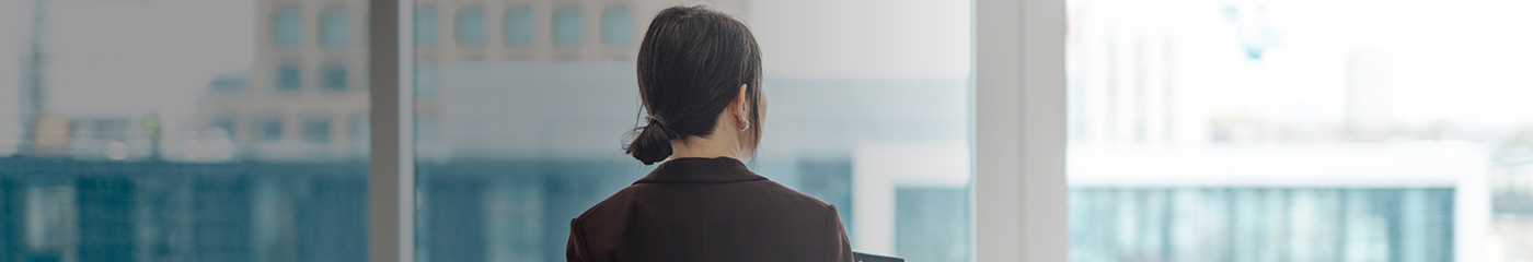 Young businesswoman with digital tablet, standing against office window with city view in modern commercial building.
