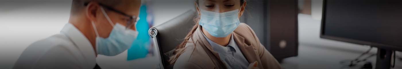 Two business professionals in the office wearing protective facemasks.