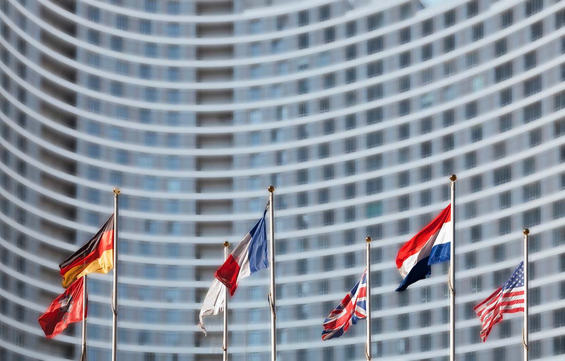 Numerous countries flags on flagpoles in front of a business building. 