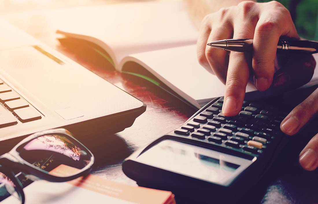 Close-up photo of a woman's hand using a calculator as she does paperwork.