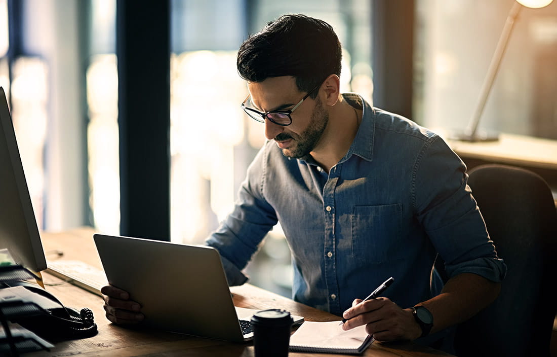 Man looking at a laptop compuer while sitting at a desk. 