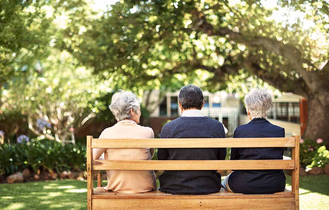Three elderly senior citizens sitting on a park bench.