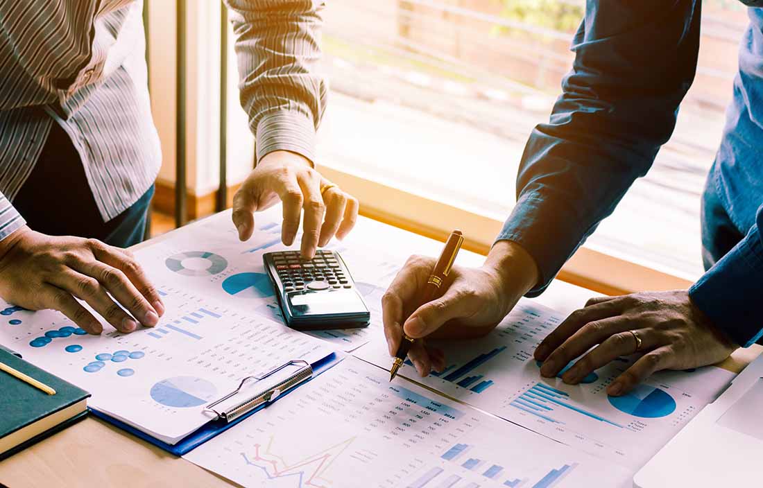 Photo of two people with pens and calculators looking over financial documents.