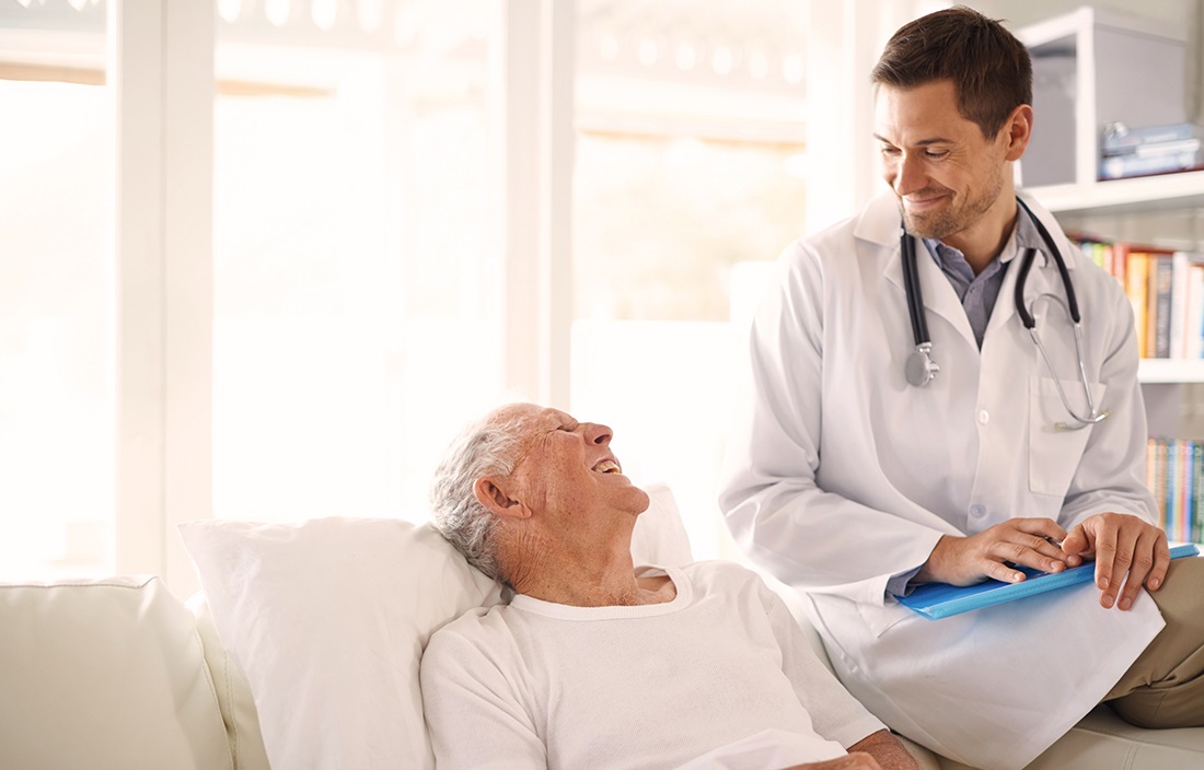 Image of smiling doctor looking down on senior patient in bed.