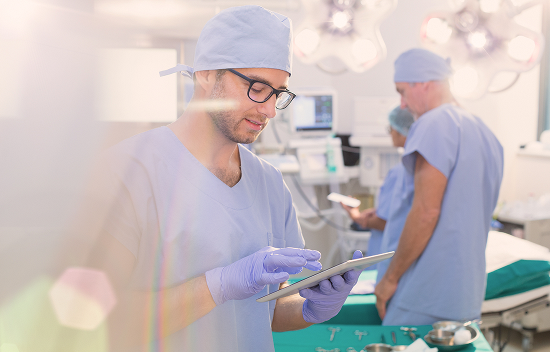 Doctor in an operating room using a handheld tablet device.