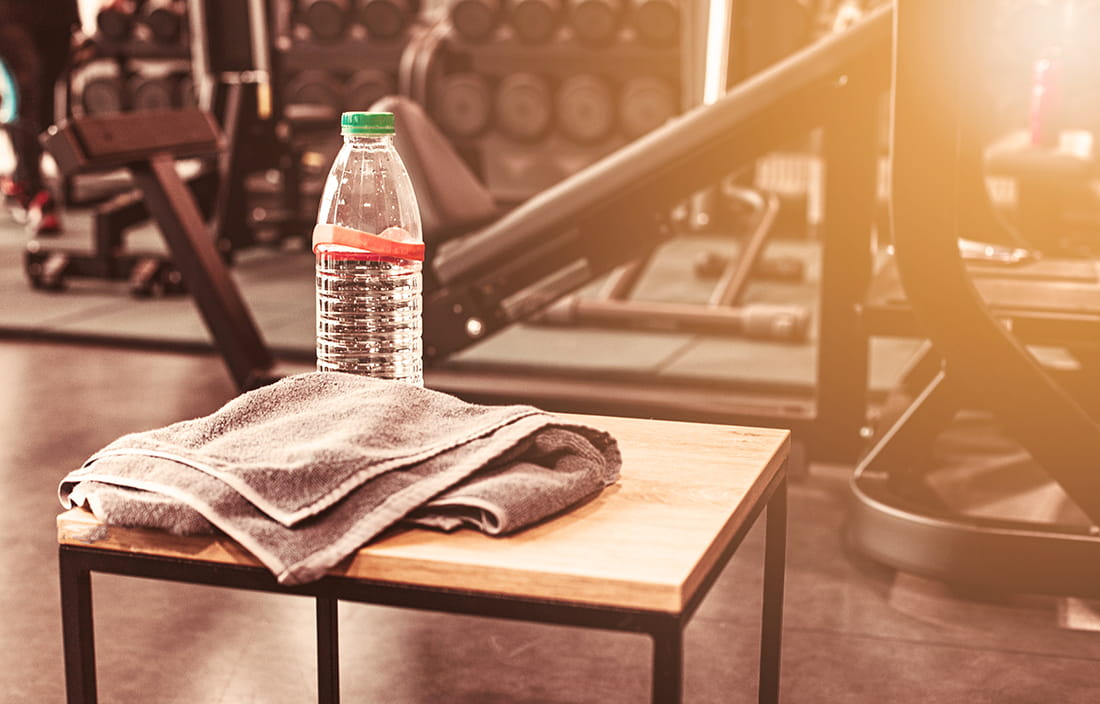 Picture of a water bottle on a bench next to gym equipment. 