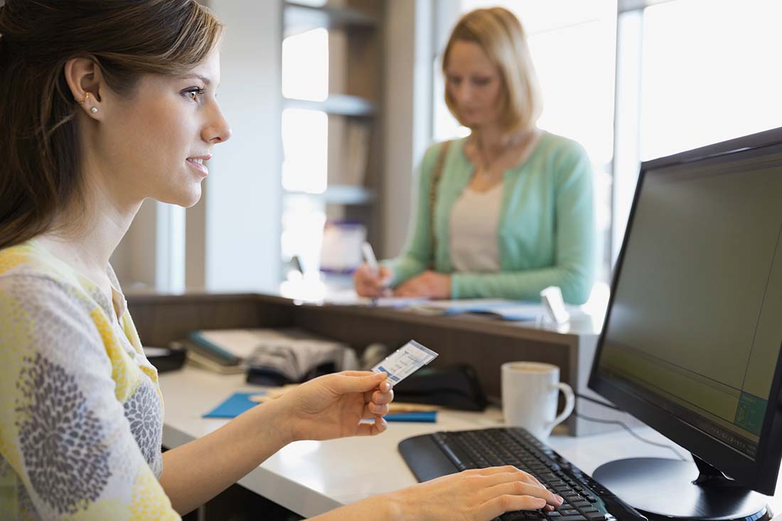 Image of receptionist holding patient insurance card in front of her computer screen.