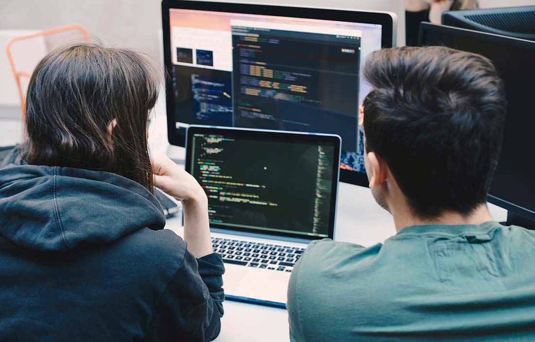 Image of a man and woman looking at a laptop screen and computer monitor.