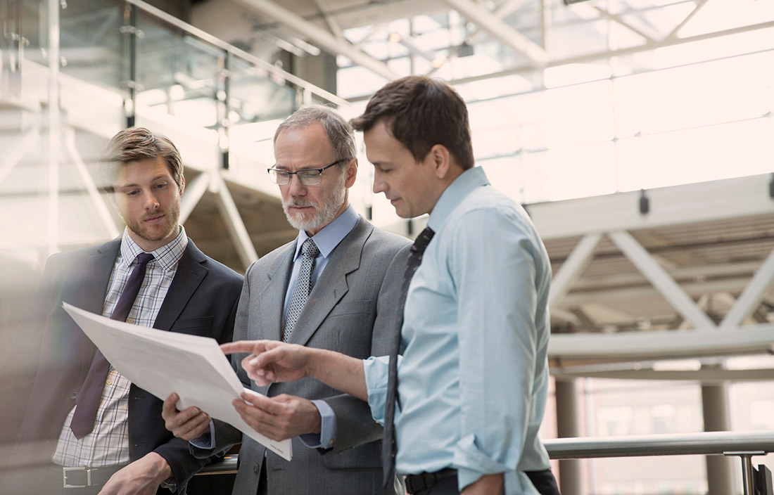 Three businessmen discussing foreign exchange risks in a factory setting. 