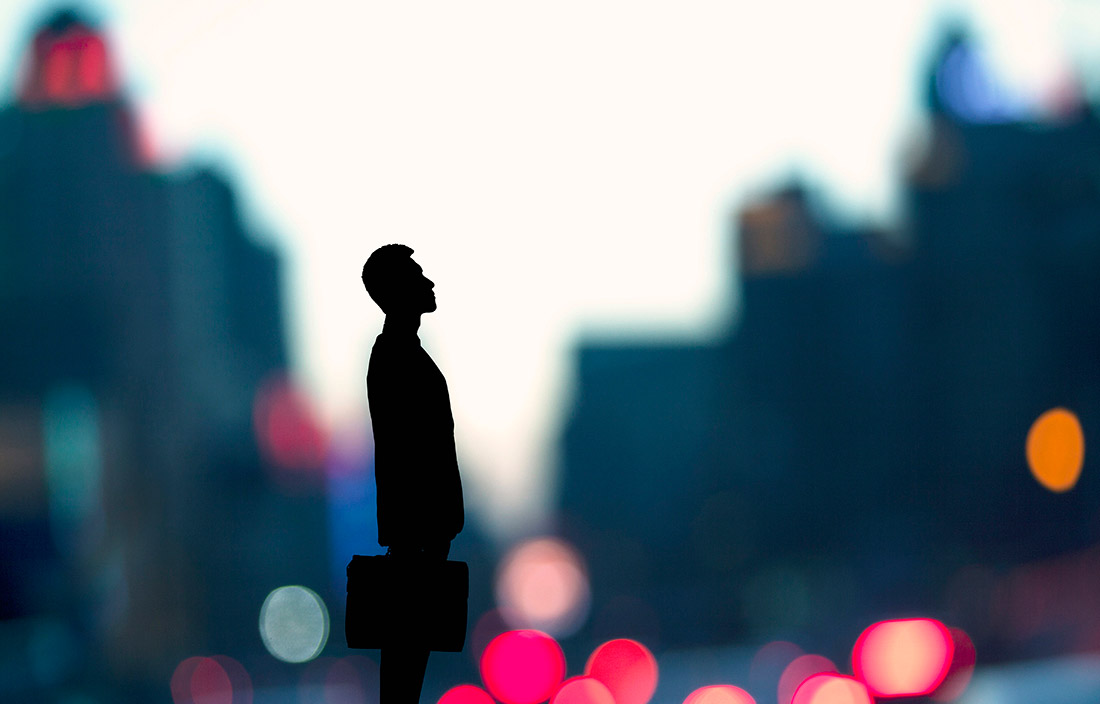 Photo of man with briefcase standing in front of blurred city scene.