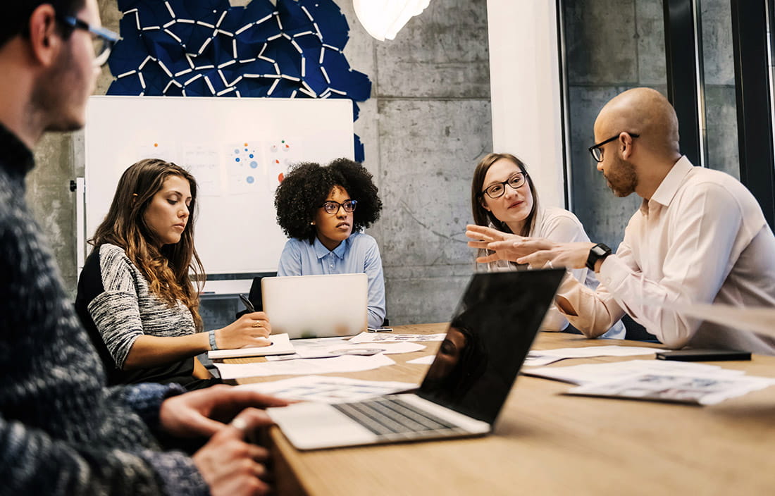 Photo of five people sitting around a meeting table in discussion. 