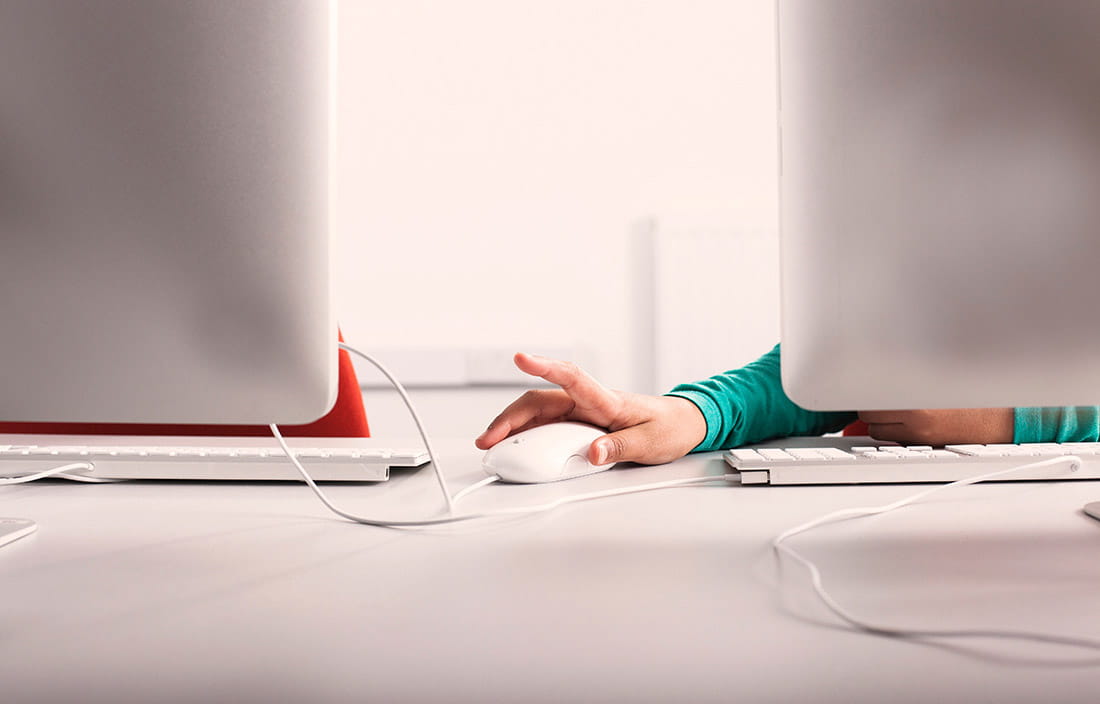 Image of person clicking mouse from behind computer. 