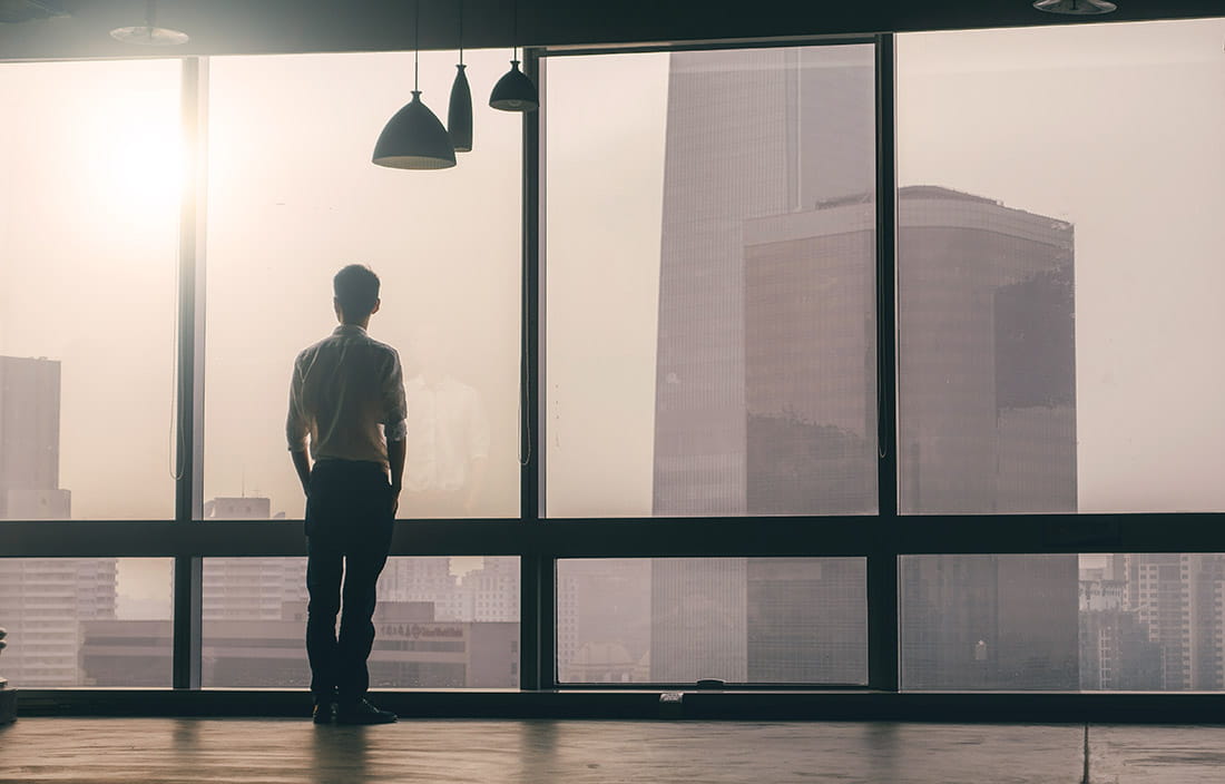 Image of a man looking out of large office windows, onto a misty city morning.