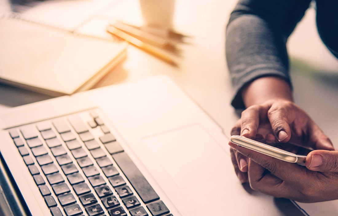 Image of person using cell phone in front of laptop