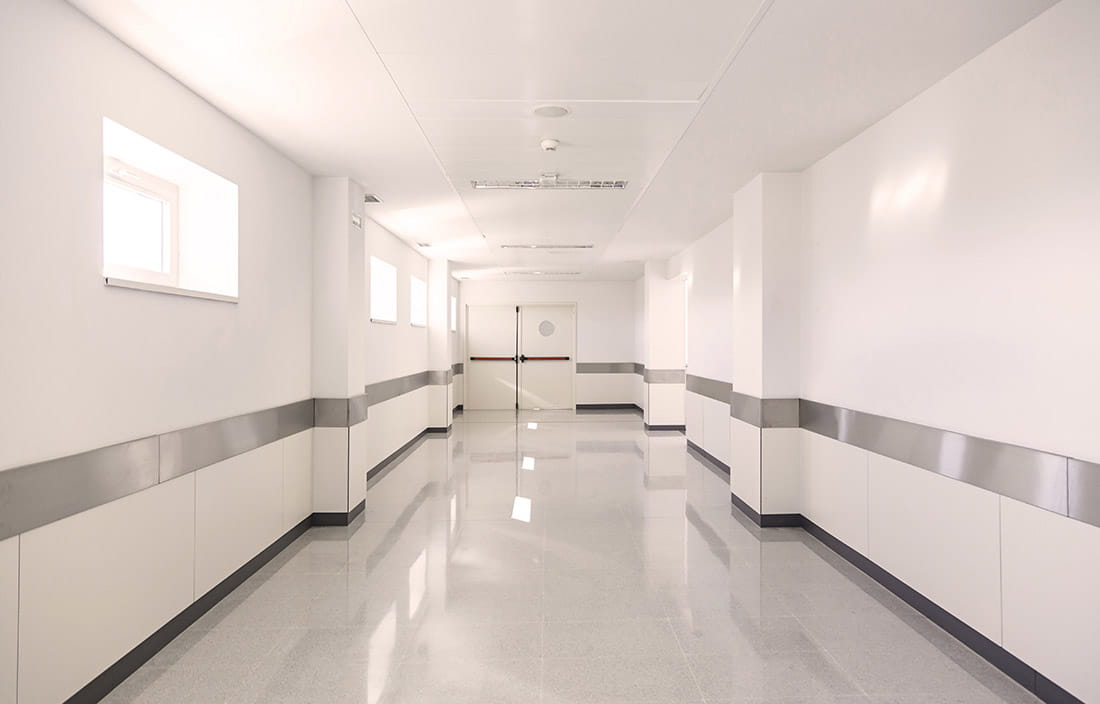 A picture of pristine, white hospital hallway leading towards two double doors. 