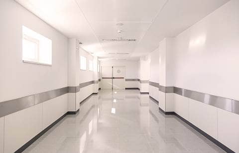 A picture of pristine, white hospital hallway leading towards two double doors.