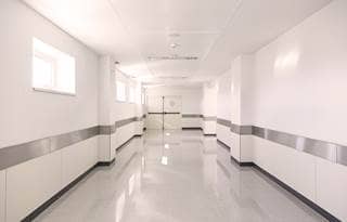 A picture of pristine, white hospital hallway leading towards two double doors.