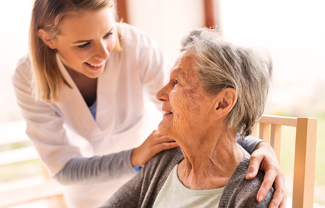 Image of a female nurse leaning over a smiling elderly woman.
