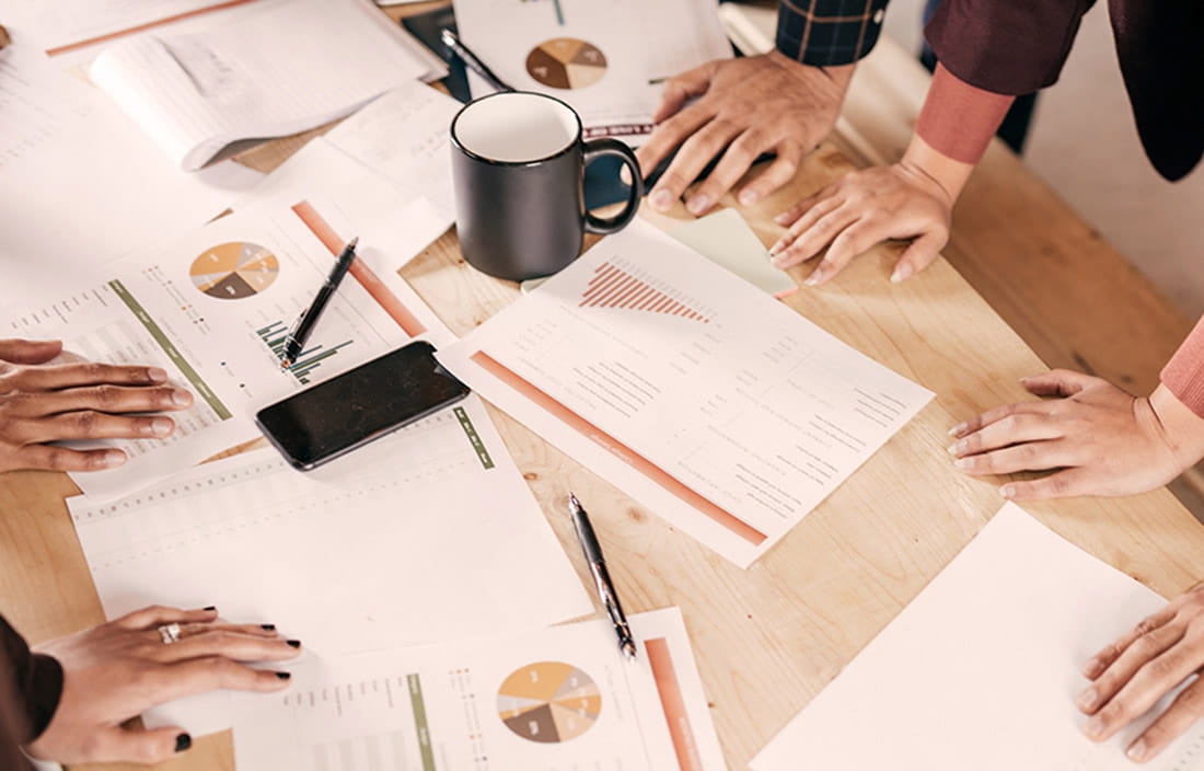 Image of hands on table full of business papers and a coffee mug. 