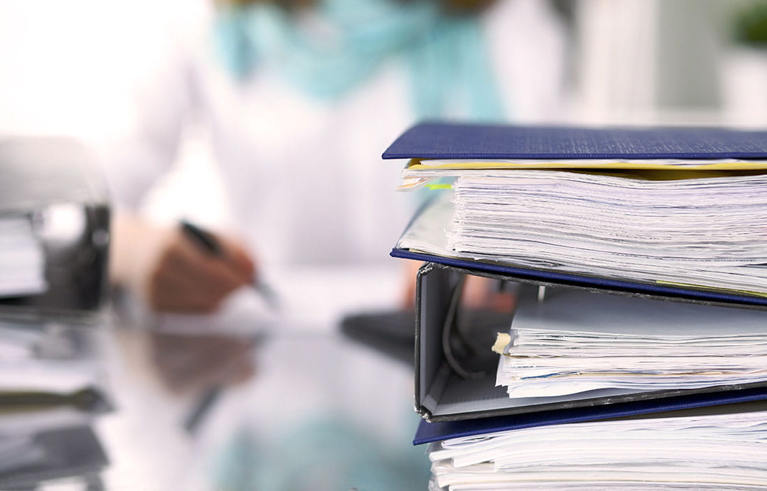 View of a stack of binders and business papers on top of a desk. 