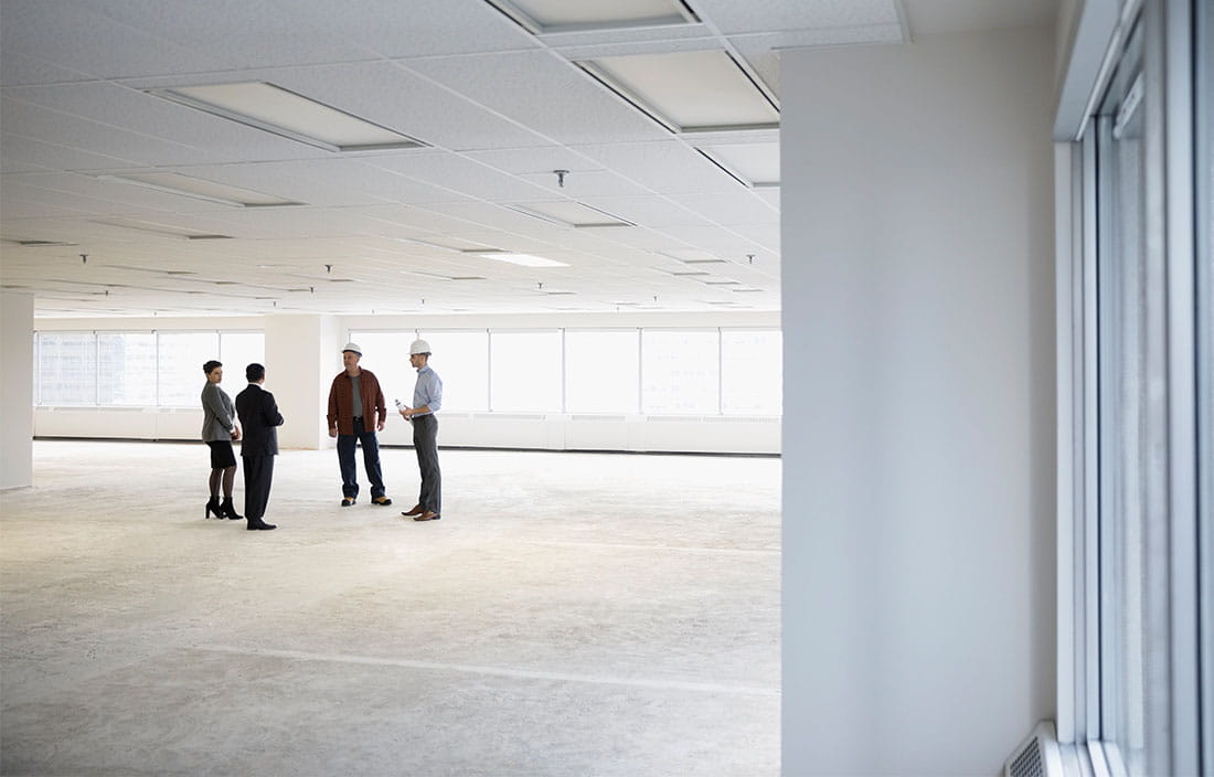 Two business professionals discussing office floor plans with two construction workers. 