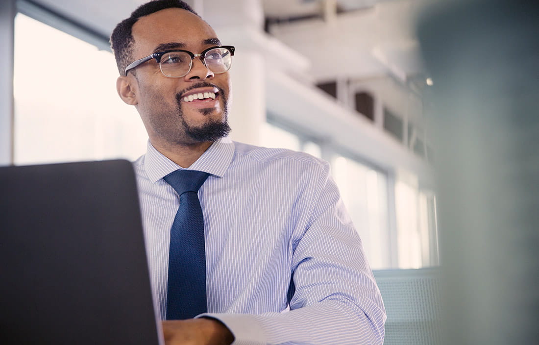 A business professional sitting with a laptop at a table and smiling.