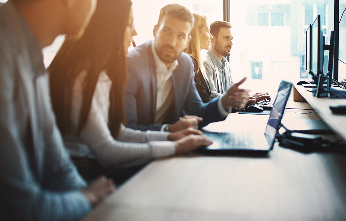 Business people talking while sitting at a desk with a laptop open.