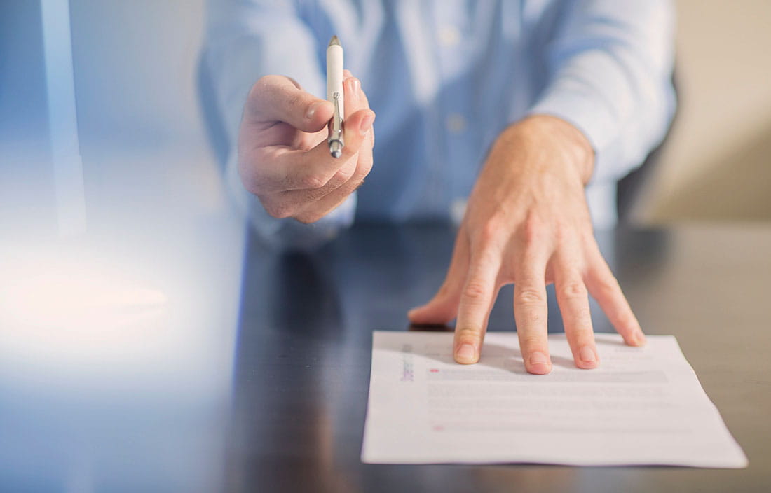 A business person with a contract on a desk and a pen in their hand. 