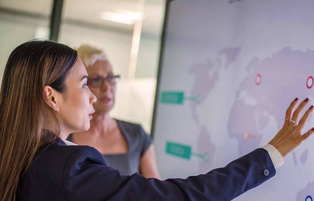 Dos compañeros de trabajo discutiendo temas de guerra comercial mientras ven un mapa mundial.