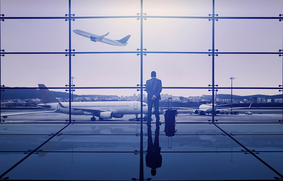 A business man looking out an airport window at a plane taking off. 
