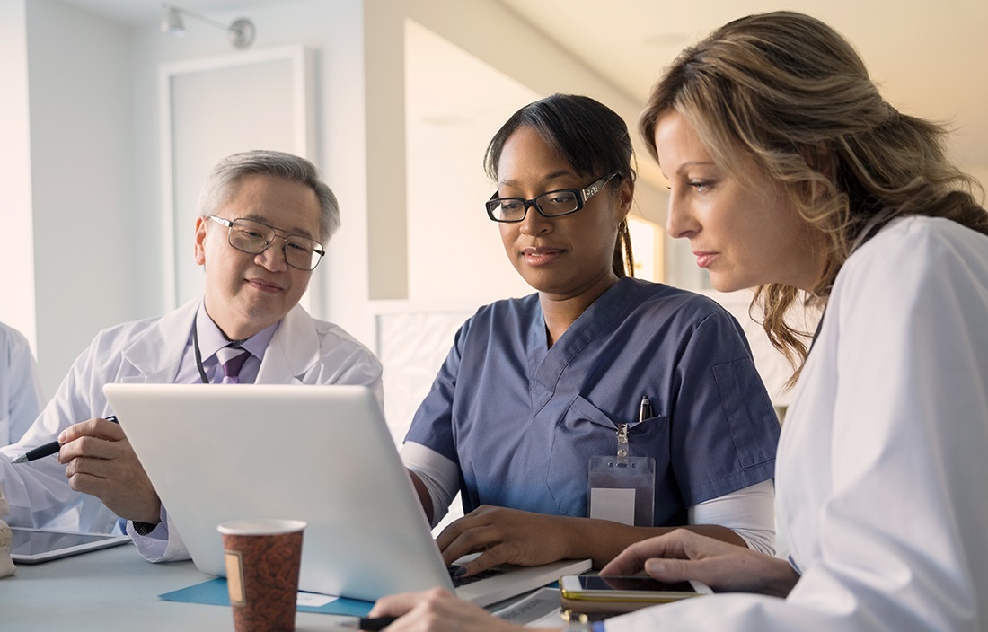 Image of three medical personnel looking at a laptop.