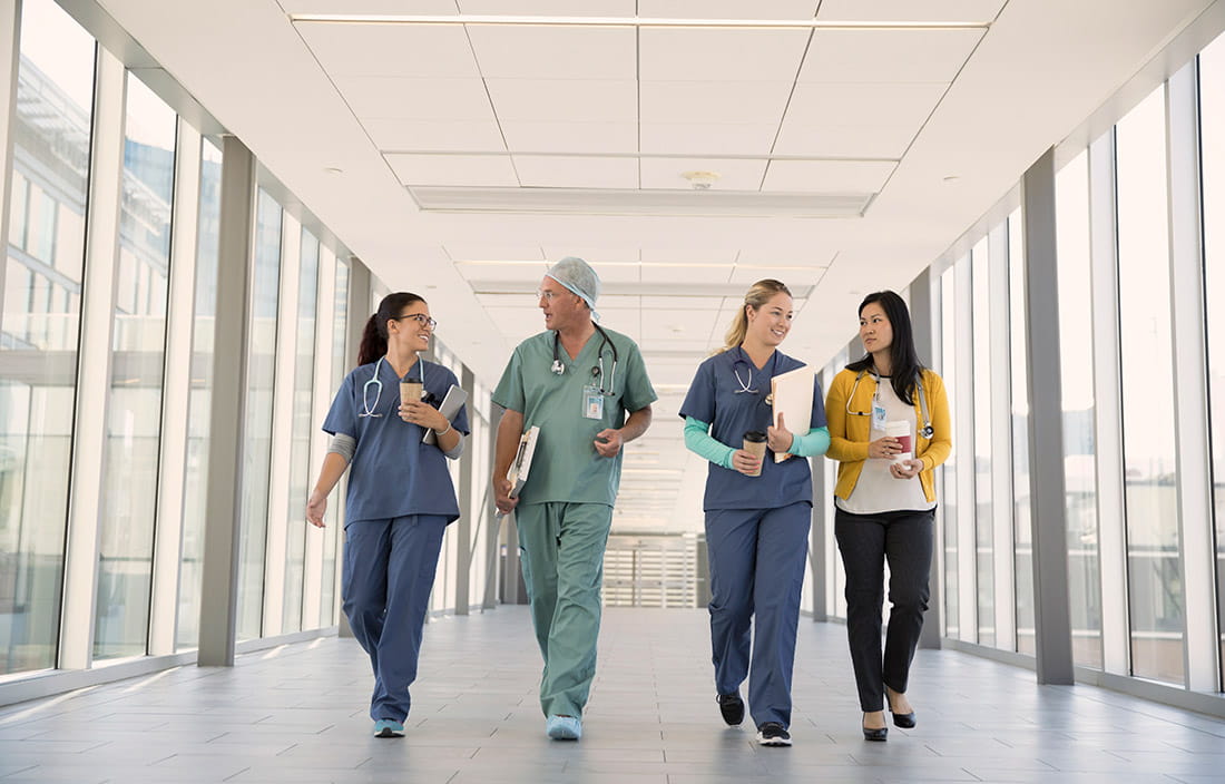 Four physicians and doctors walking down a glass hallway corridor.