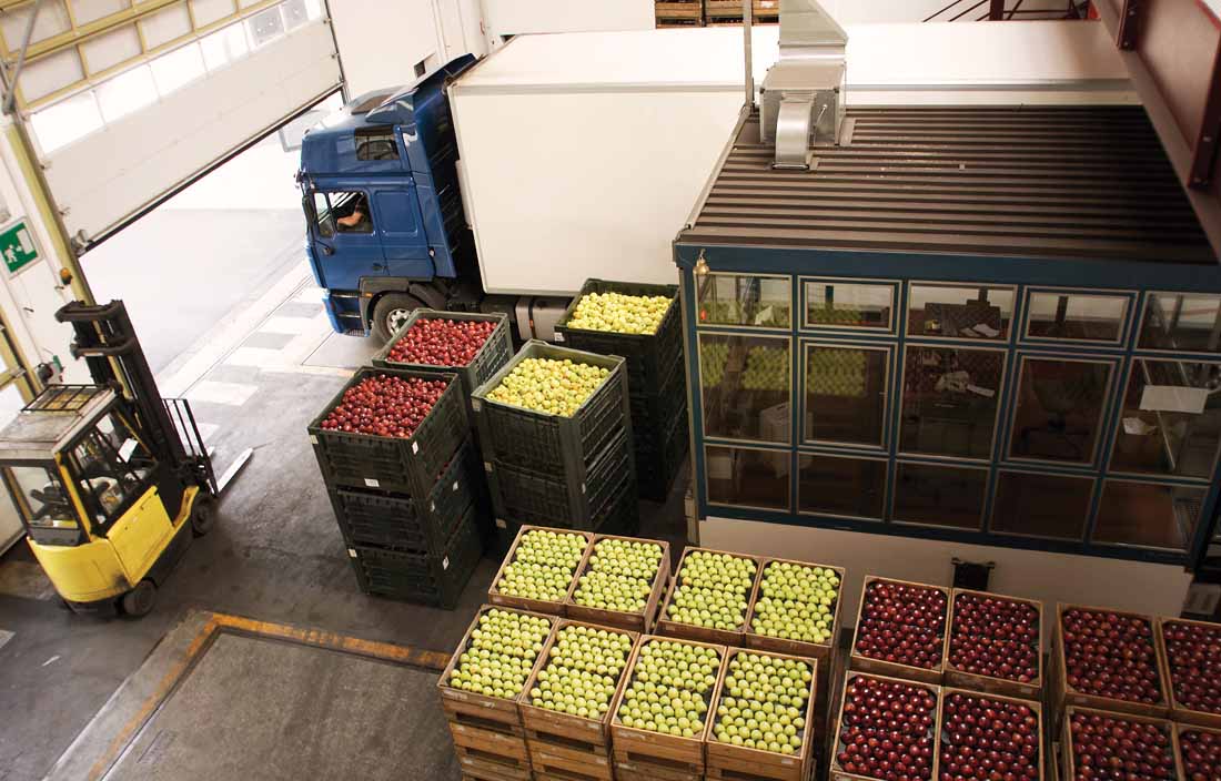 Interior of a warehouse with a shipping truck next to cartons and pallets of apple produce shipments.