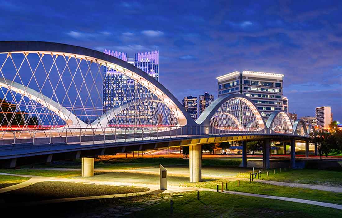 Image of a bridge that is lit up at night with the city in the background.