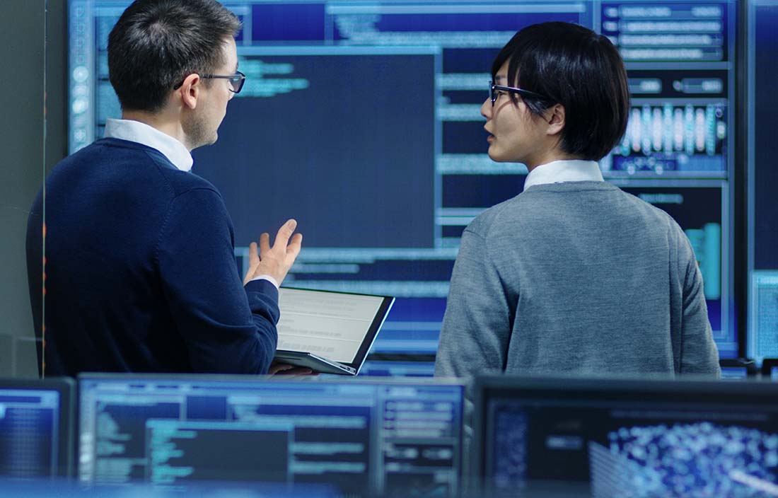Two people surrounded by computers, discussing cyber security threats