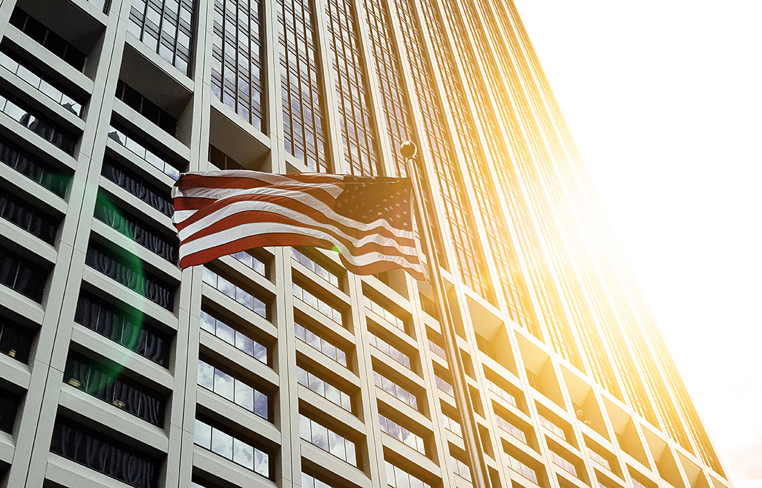 Image of American flag flying in front of a skyscraper.
