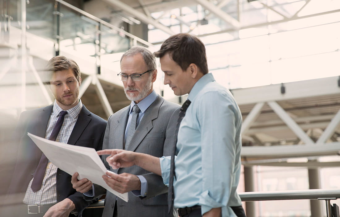 Three businessmen looking at plans to optimize their internal audit with quality assurance review.