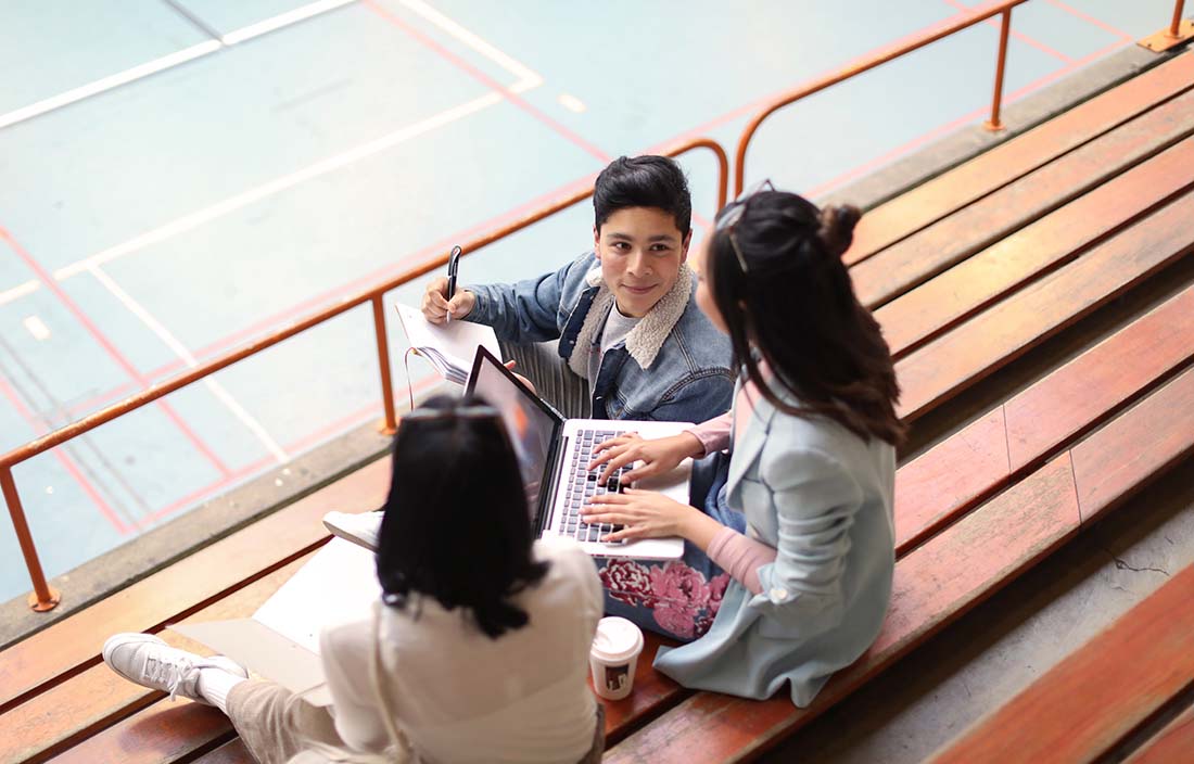 A group of students gather around a laptop during a break.