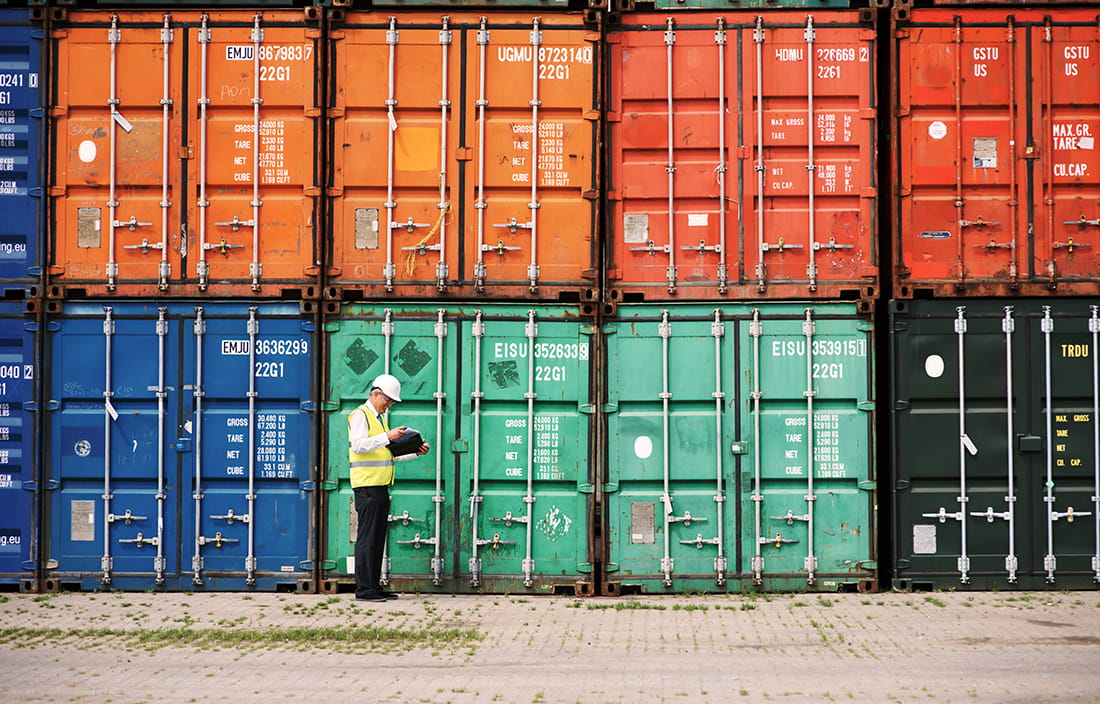 Shipping worker standing in front of a stack of metal cargo crates. 