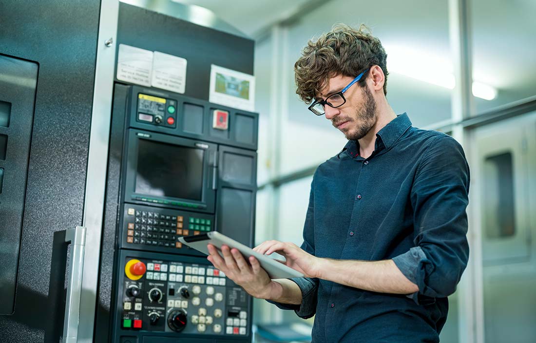 Worker standing next to machinery while using a tablet handheld device.