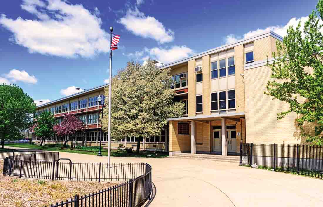 Three-story school building with an American flag in the front courtyard. 
