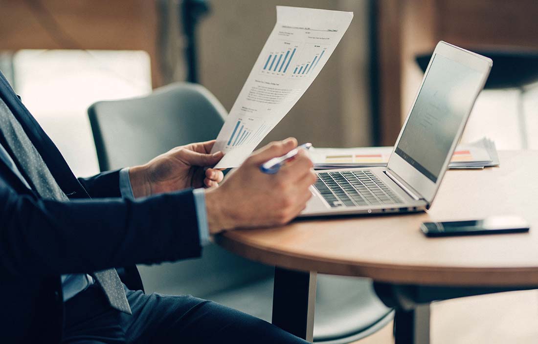 Man sitting at a table with a laptop reading a report