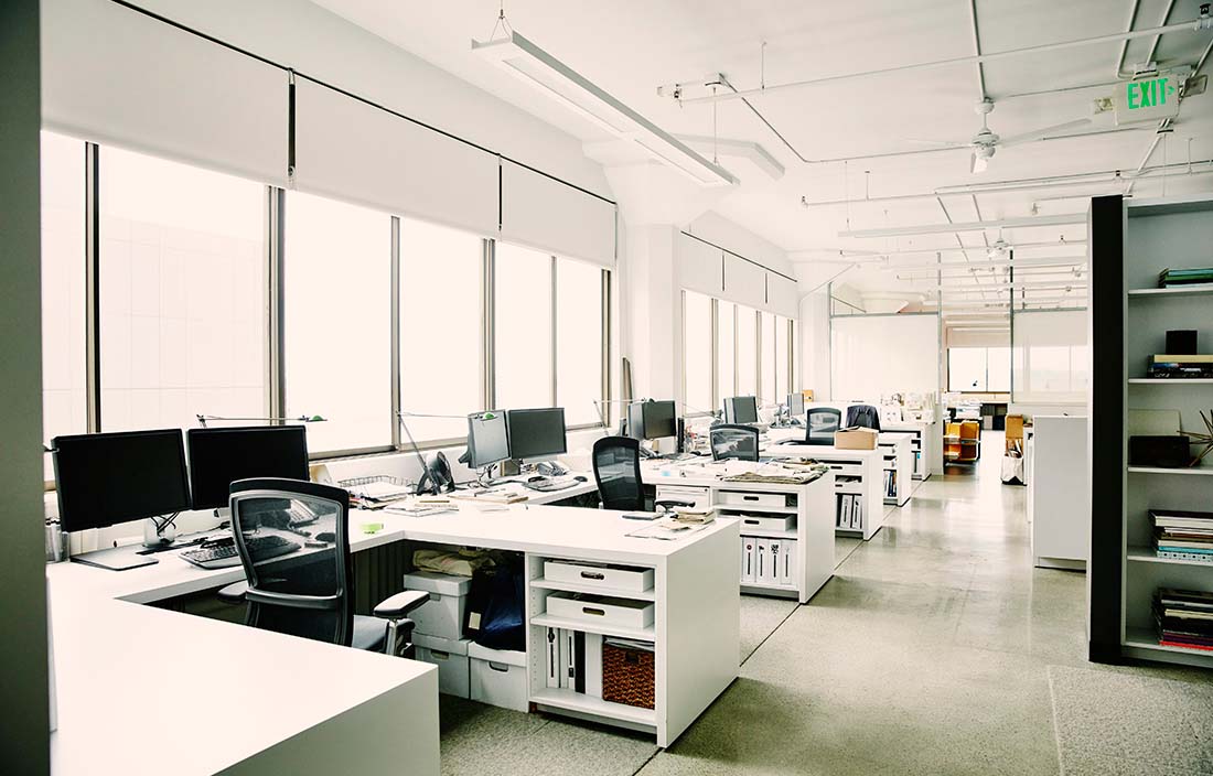 An empty modern office during the day with desk on the left hand side lining the window. 