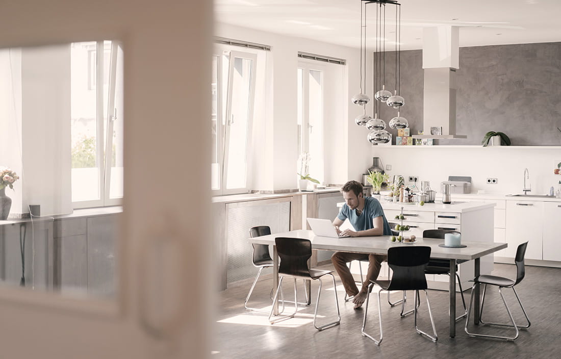 Man wearing no shoes sitting in a very modern kitchen using his laptop computer.