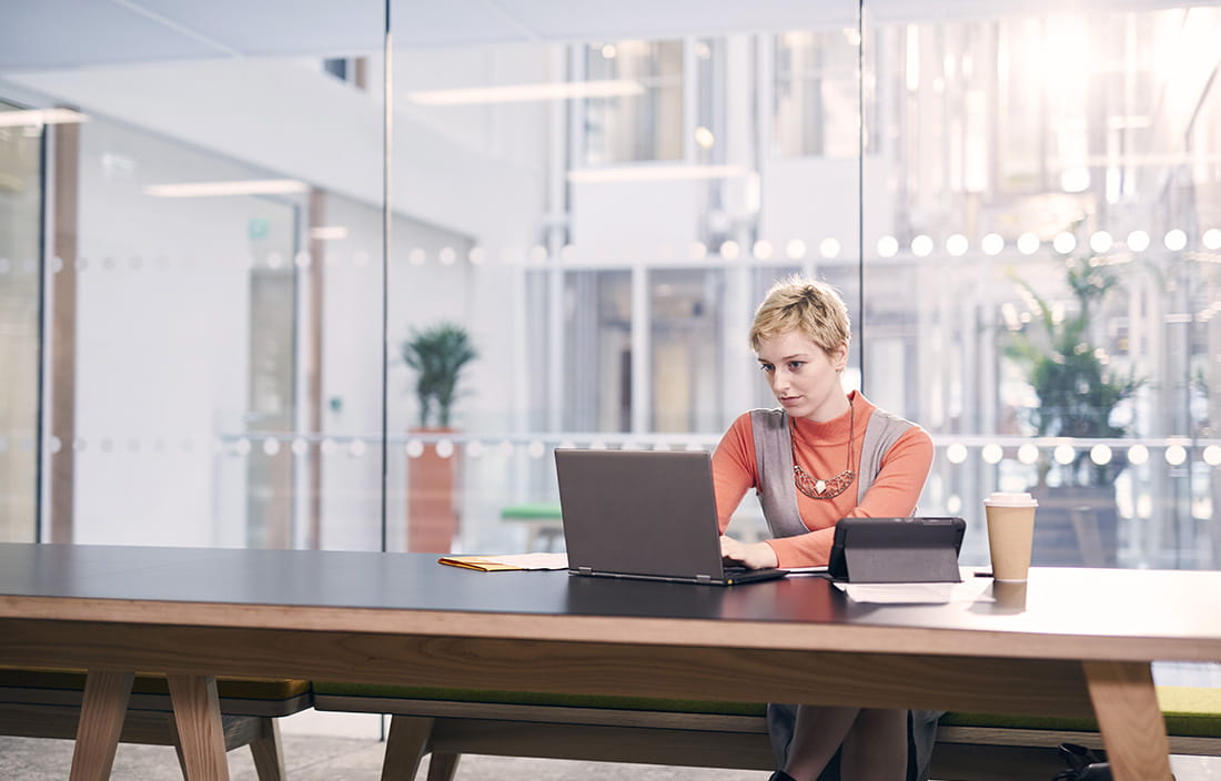 Young woman sitting at modern table and lounge area using her laptop computer. 