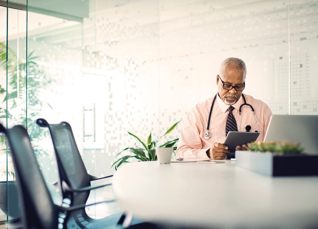 Doctor sitting at a table looking at a tablet.