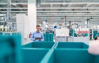 Factory worker inspecting work stations and factory lines with a tablet in his hand.