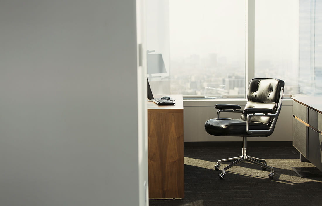 View of an office doorway with a black leather chair in the sunlight. 