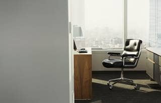 View of an office doorway with a black leather chair in the sunlight.